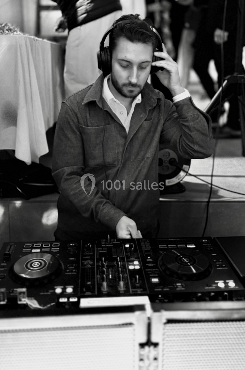 Un DJ portant un casque ajuste une platine lors d'un événement en intérieur.