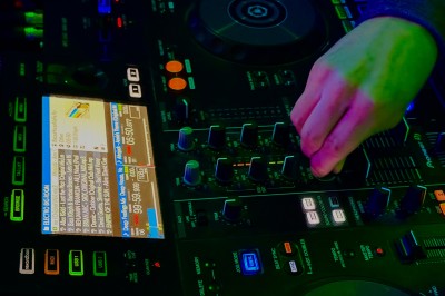 Main ajustant les réglages sur une table de mixage DJ illuminée par des lumières colorées.