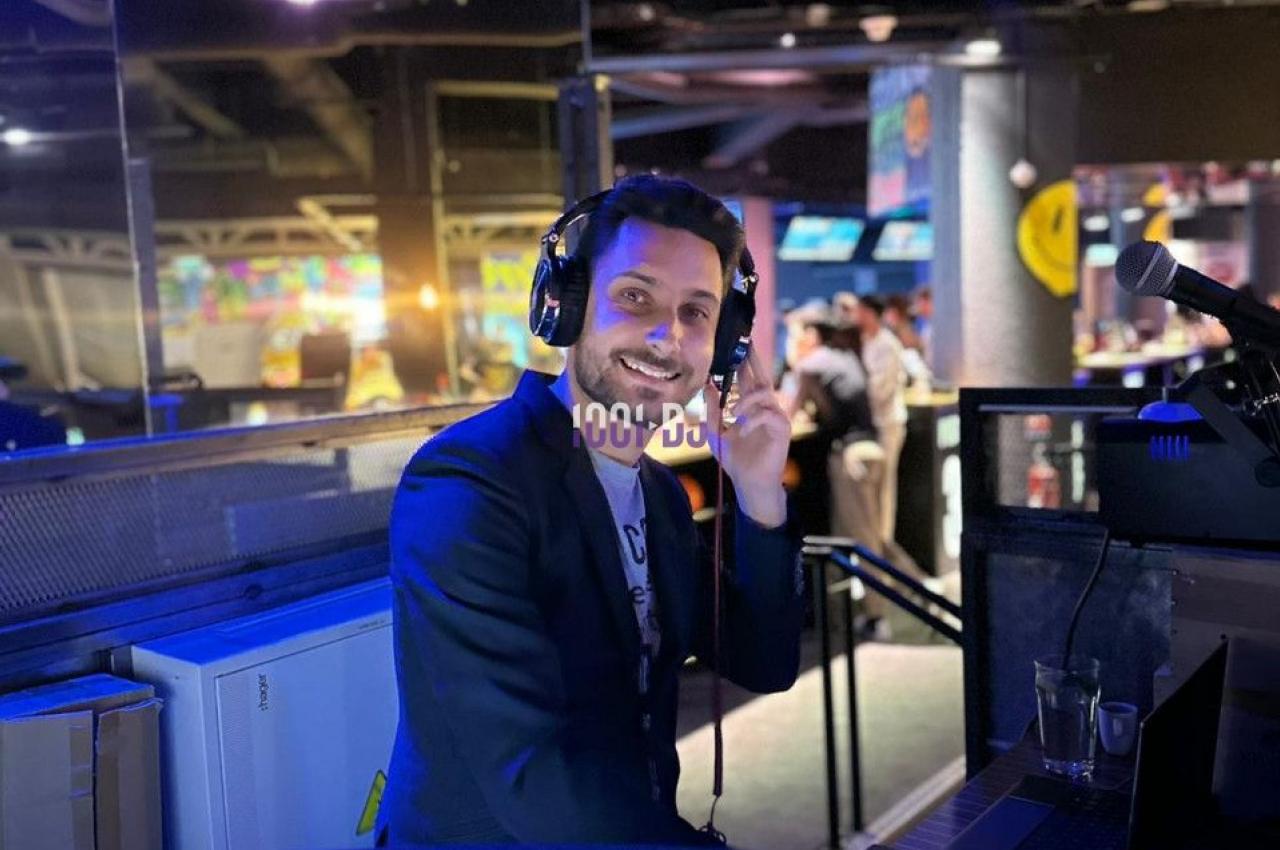 Un DJ souriant mixe de la musique dans un espace intérieur éclairé par des lumières colorées.