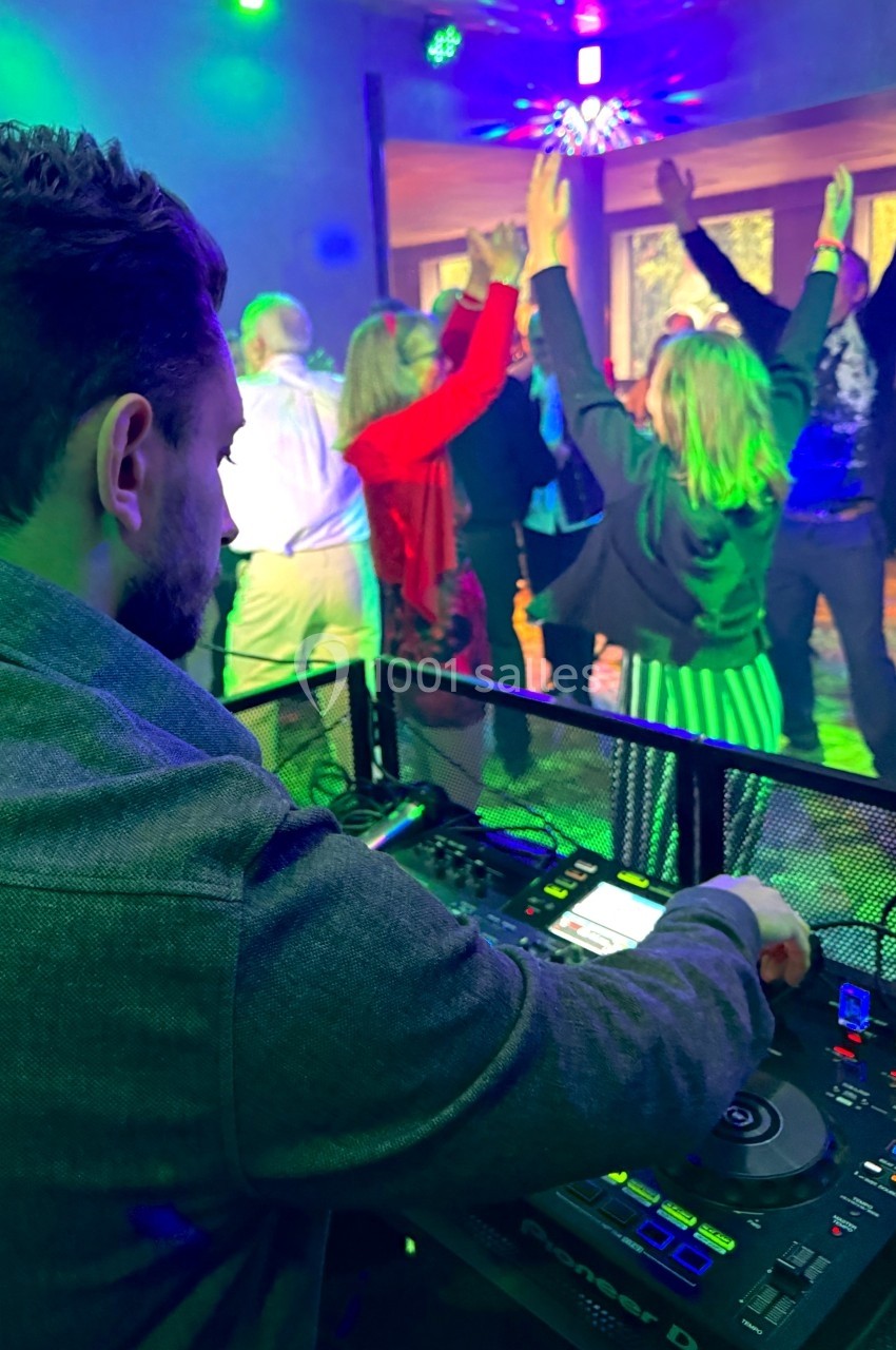 Un DJ mixe de la musique pendant que des personnes dansent sous des lumières colorées dans une salle festive.