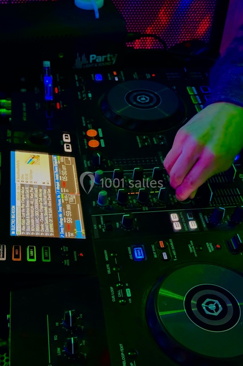 Main ajustant des réglages sur une table de mixage DJ lumineuse avec des écrans et des boutons colorés.