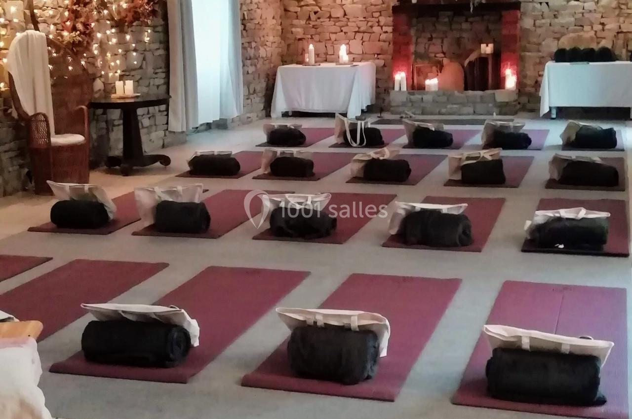Salle aménagée pour une séance de méditation avec des tapis et coussins alignés sur un sol en pierre, éclairage tamisé.