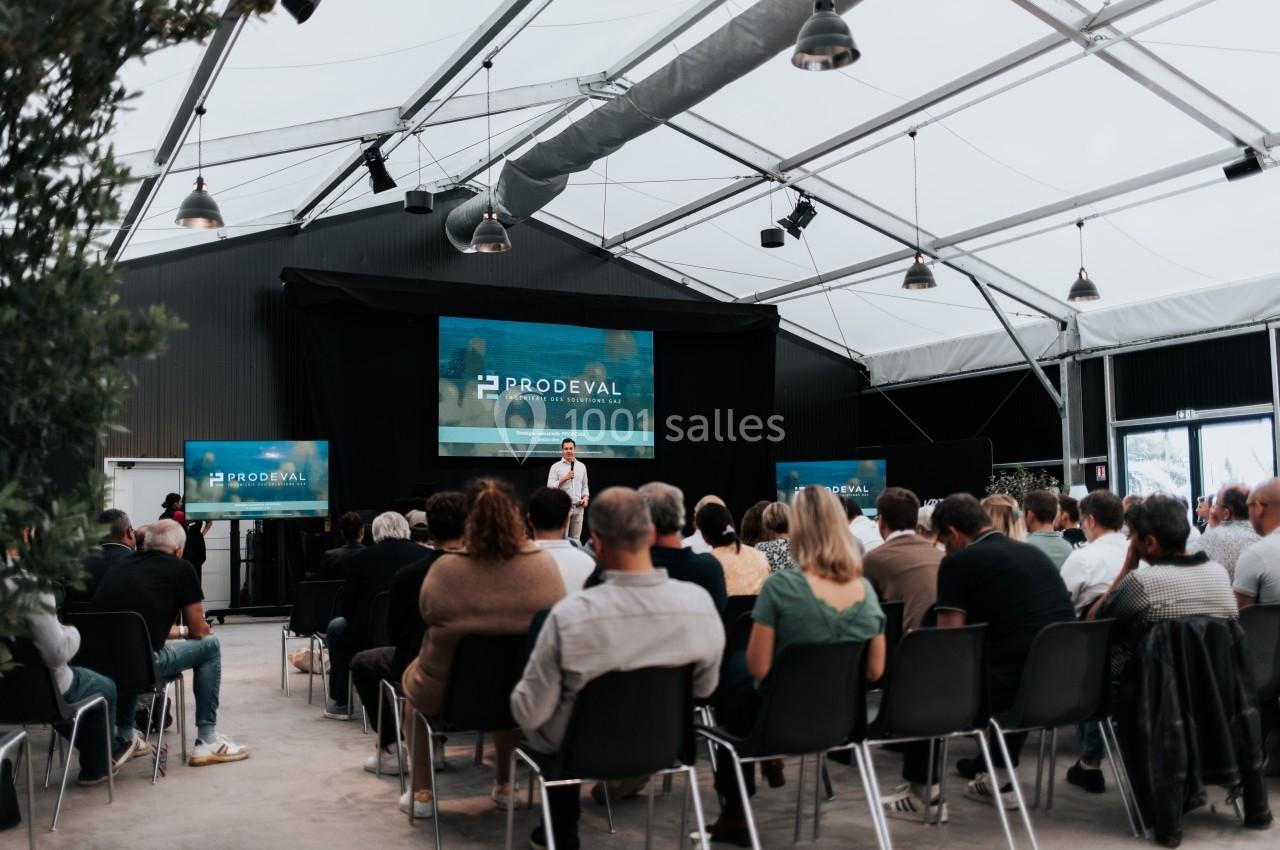 Un conférencier s'adresse à un public assis dans une salle lumineuse avec des écrans affichant ’Prodeval’.