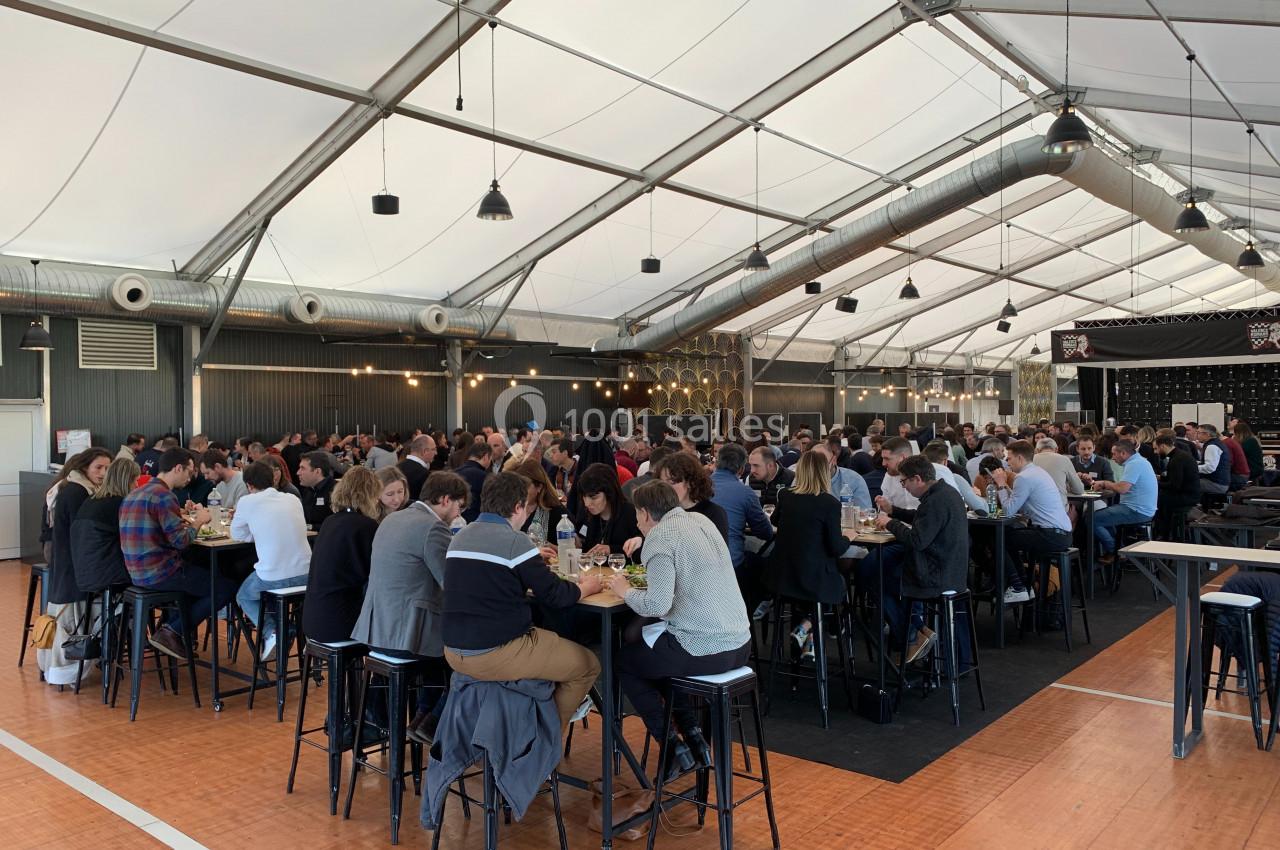 Des personnes assises à des tables hautes dans une grande salle lumineuse sous une structure en toile tendue.