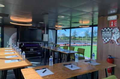 Groupe de personnes rassemblées sous une tente lors d'un événement en extérieur, près d'un bâtiment moderne.