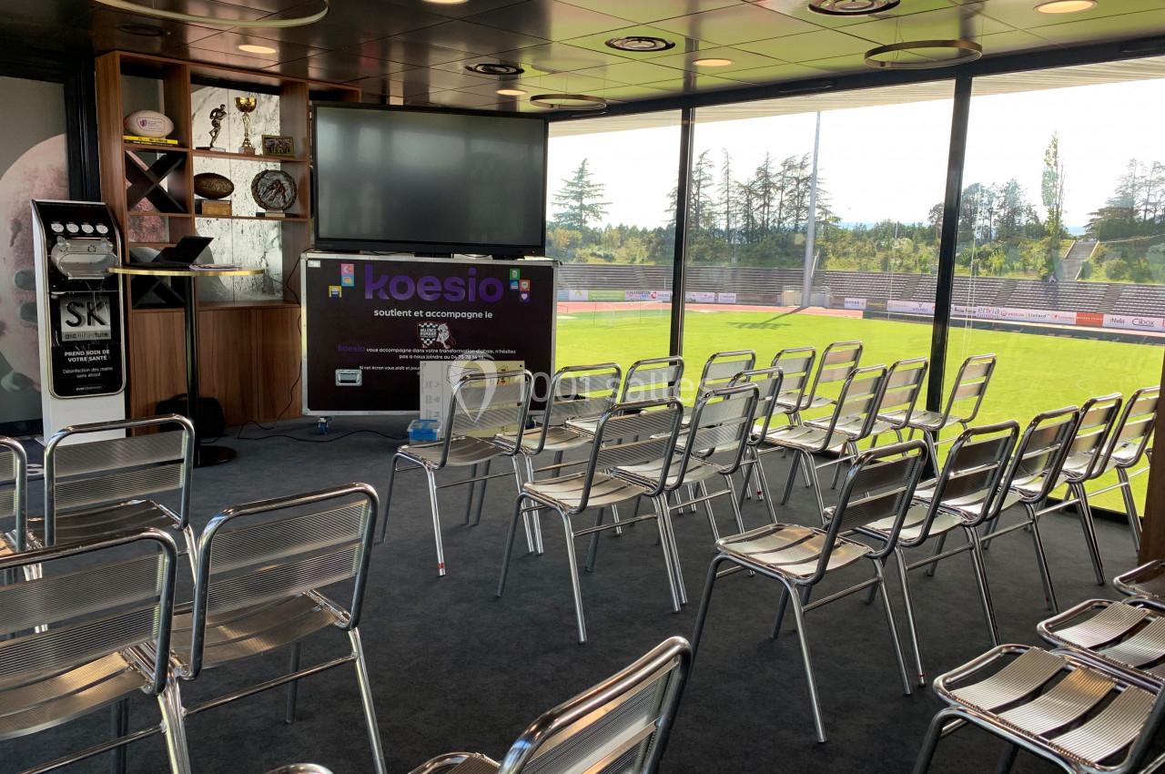 Salle de conférence lumineuse avec des chaises alignées, un écran de présentation et une vue sur un terrain extérieur.