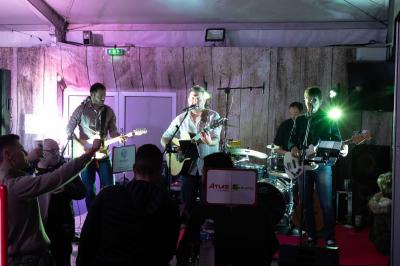 Groupe de personnes rassemblées sous une tente lors d'un événement en extérieur, près d'un bâtiment moderne.