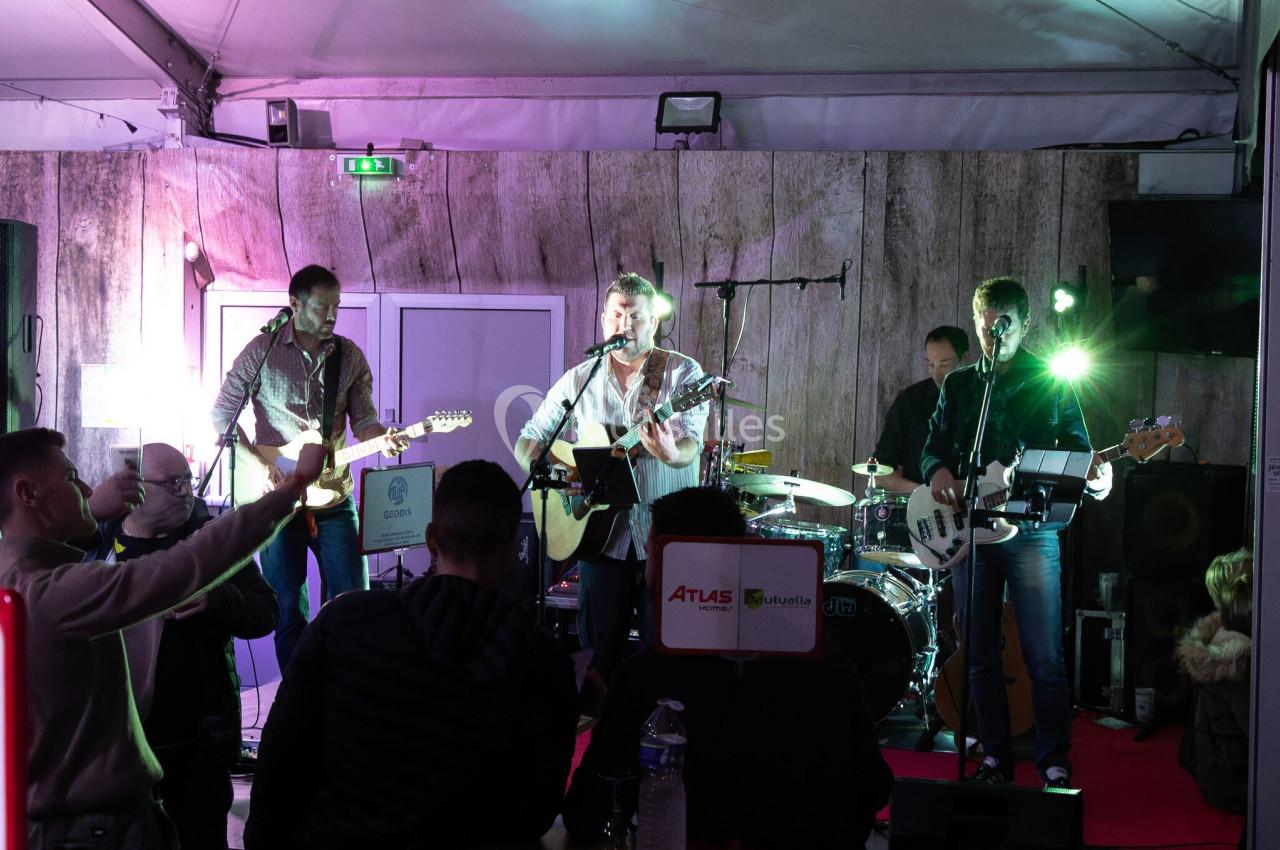 Un groupe de musiciens joue sur une scène éclairée devant un public dans un espace couvert.
