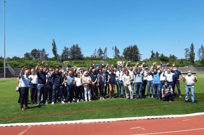 Groupe de personnes rassemblées sous une tente lors d'un événement en extérieur, près d'un bâtiment moderne.