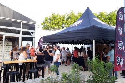 Groupe de personnes rassemblées sous une tente lors d'un événement en extérieur, près d'un bâtiment moderne.