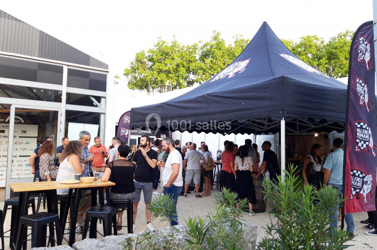 Groupe de personnes rassemblées sous une tente lors d'un événement en extérieur, près d'un bâtiment moderne.