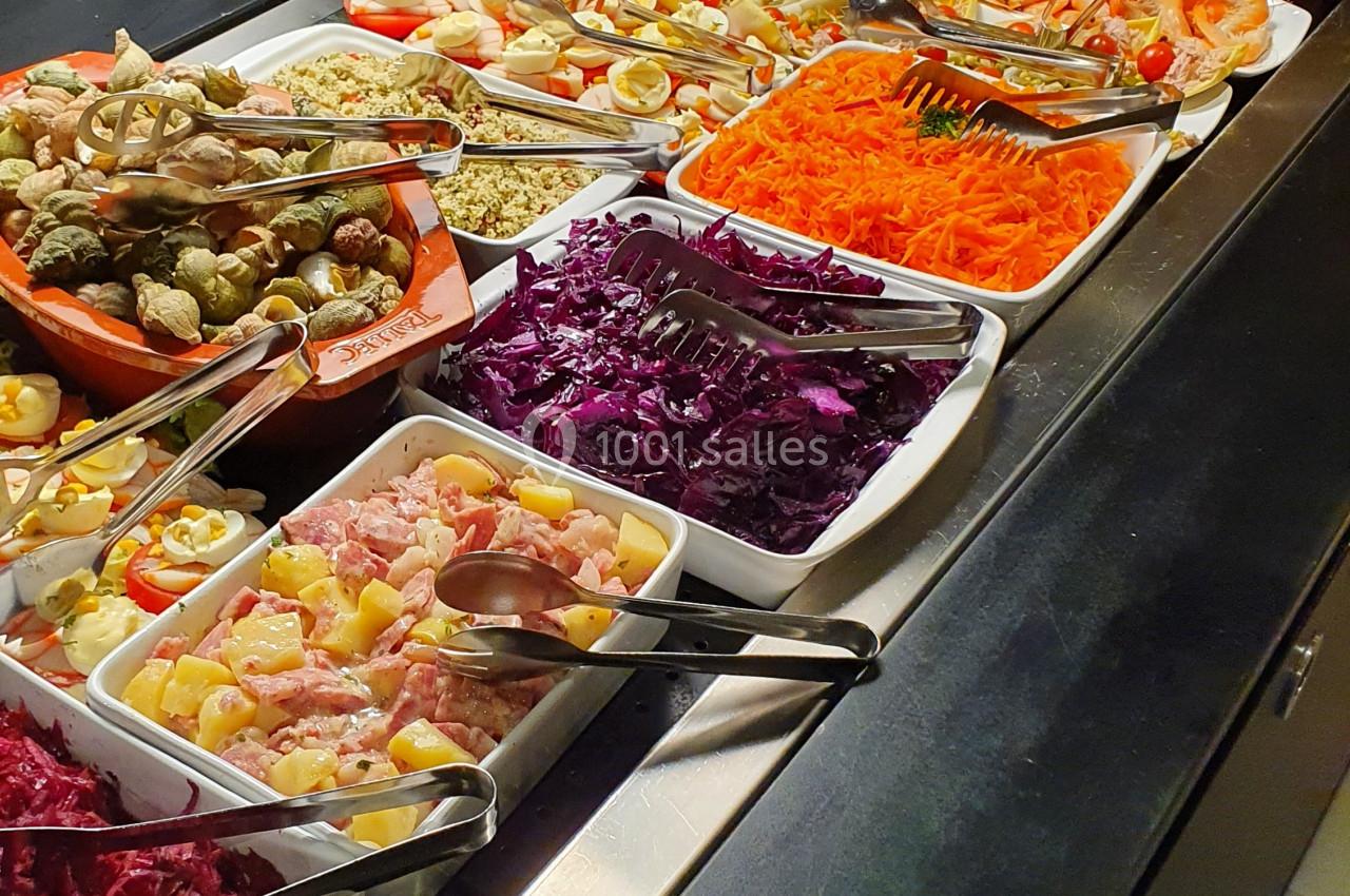 Buffet varié avec salades, légumes, charcuteries et condiments disposés dans des plats sur un comptoir.