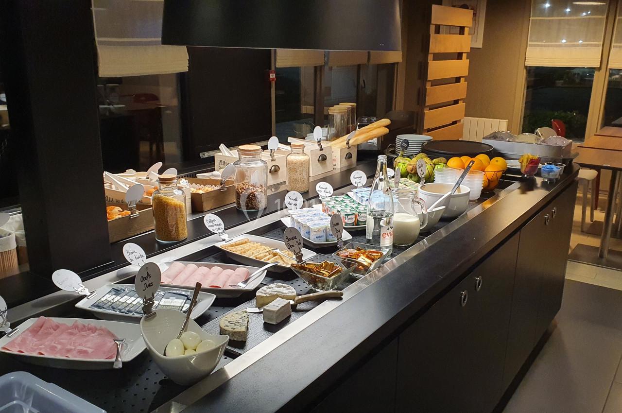 Buffet de petit-déjeuner avec une variété d'aliments, dont charcuterie, fromage, céréales, fruits et boissons.