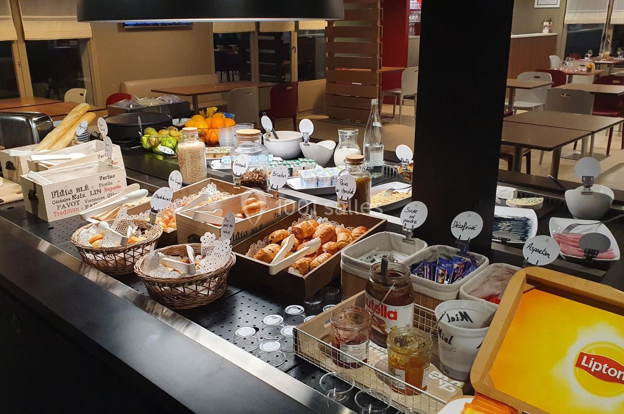 Buffet de petit-déjeuner avec viennoiseries, fruits, céréales, boissons et condiments dans une salle de restaurant.