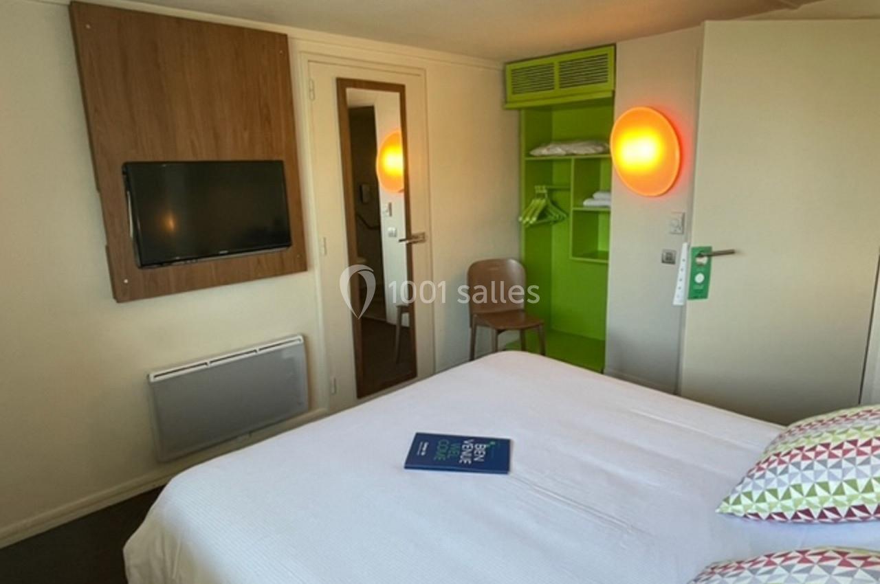 Chambre d'hôtel avec lit double, télévision murale, espace de rangement vert et éclairage mural.