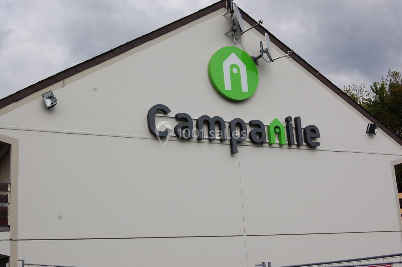 Façade d'un bâtiment avec le logo et l'enseigne ’Campanile’ sur un mur blanc sous un ciel nuageux.