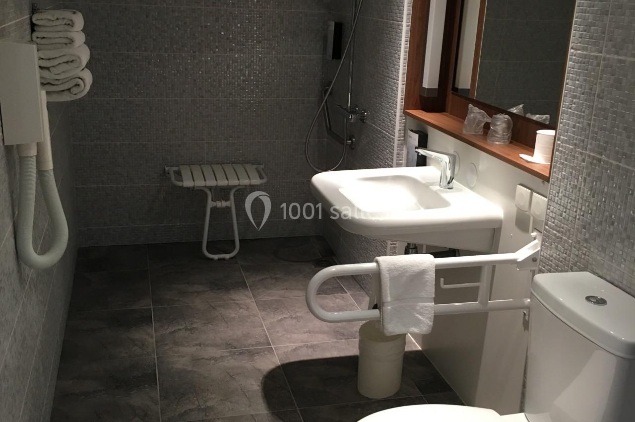 Salle de bain accessible avec douche à l'italienne, barre d'appui, lavabo, toilettes et carrelage gris.