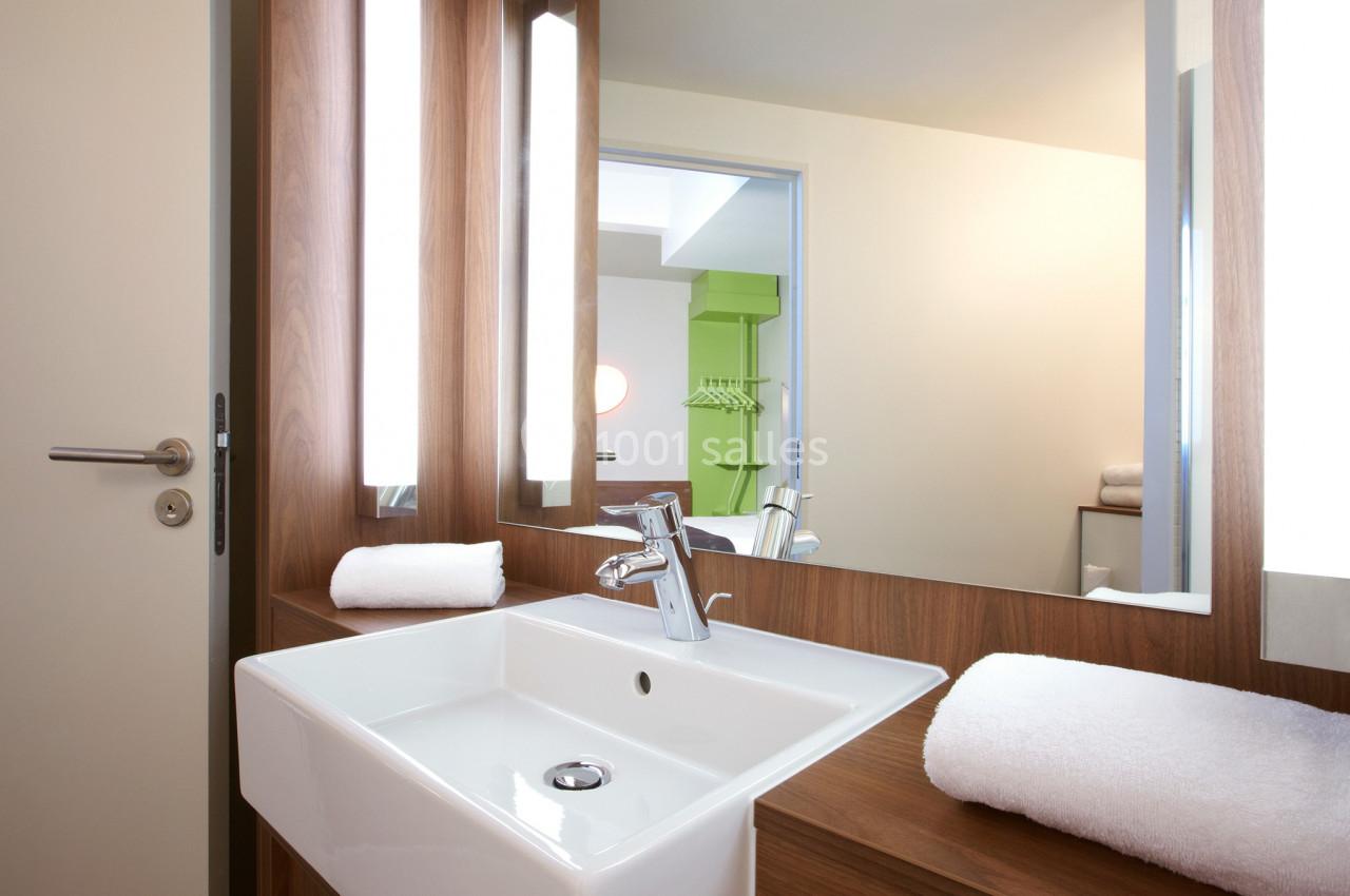 Lavabo blanc avec robinet chromé intégré dans un meuble en bois, entouré de miroirs et éclairages verticaux.