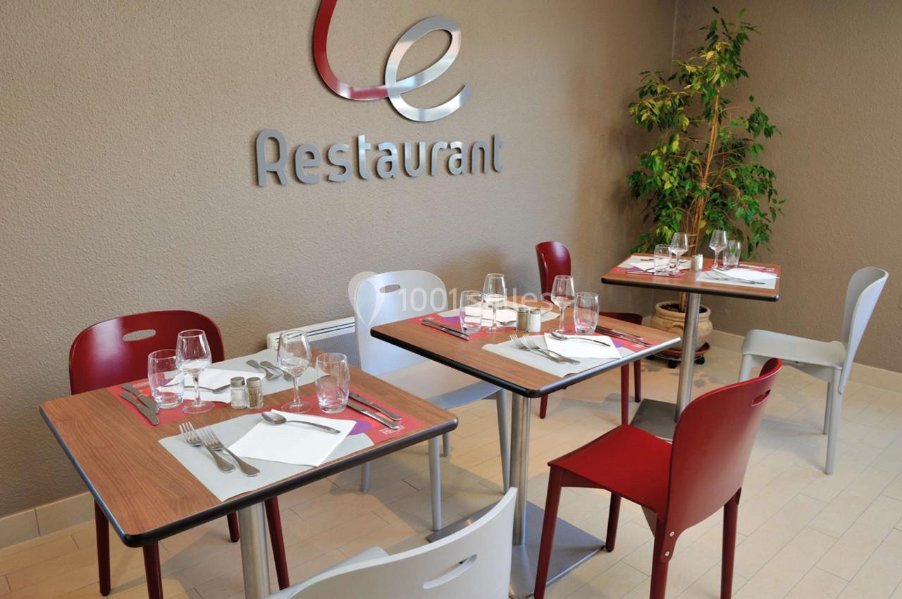 Salle de restaurant avec tables dressées, chaises colorées et plante verte en arrière-plan.