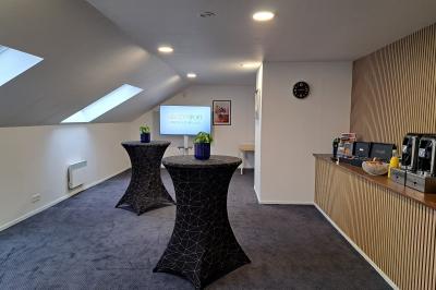 Salle de réunion lumineuse avec table rectangulaire, chaises colorées, écran, paperboard et coin café en arrière-plan.