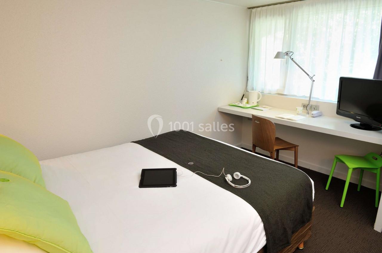 Chambre d'hôtel lumineuse avec un lit double, un bureau équipé d'une lampe, une chaise et une télévision.