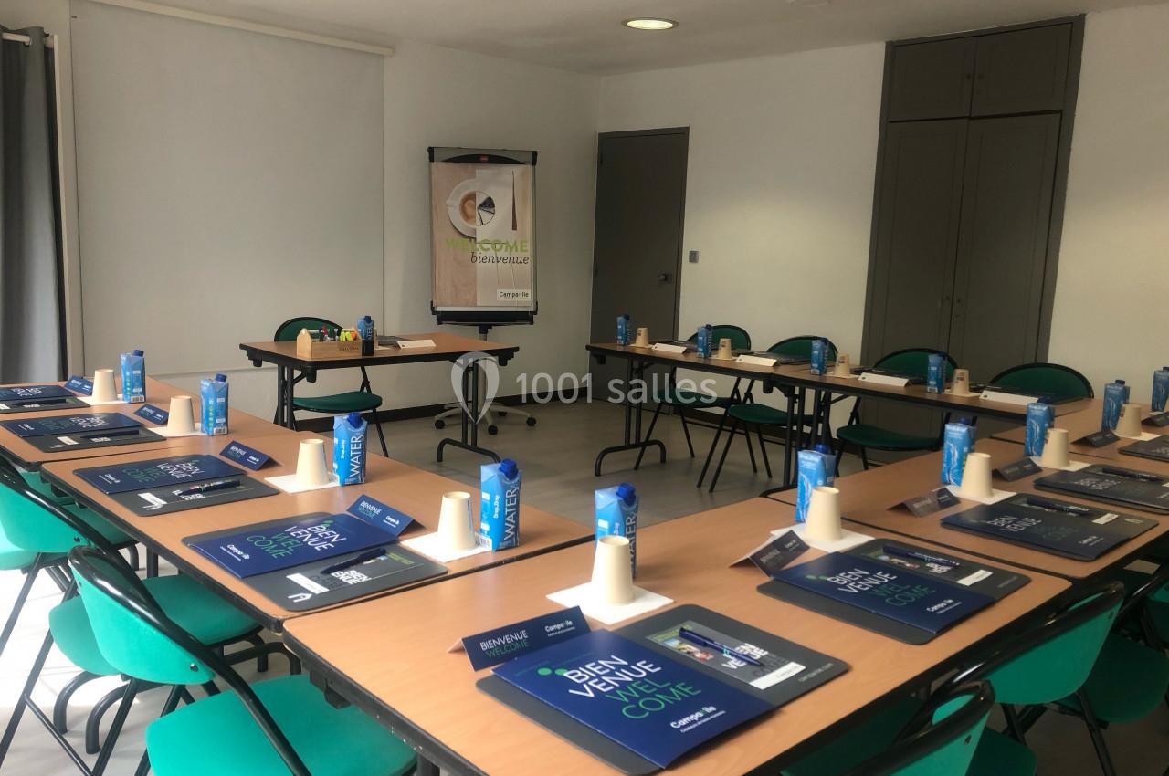 Salle de réunion aménagée avec des tables disposées en U, des chaises, des blocs-notes et des bouteilles d'eau.