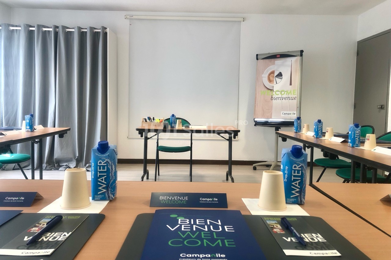 Salle de réunion préparée avec des tables disposées en U, blocs-notes, stylos, bouteilles d'eau et affiches de bienvenue.