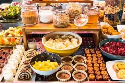 Buffet varié avec fruits frais, pâtisseries, yaourts, céréales et pots de confiture disposés sur une table.