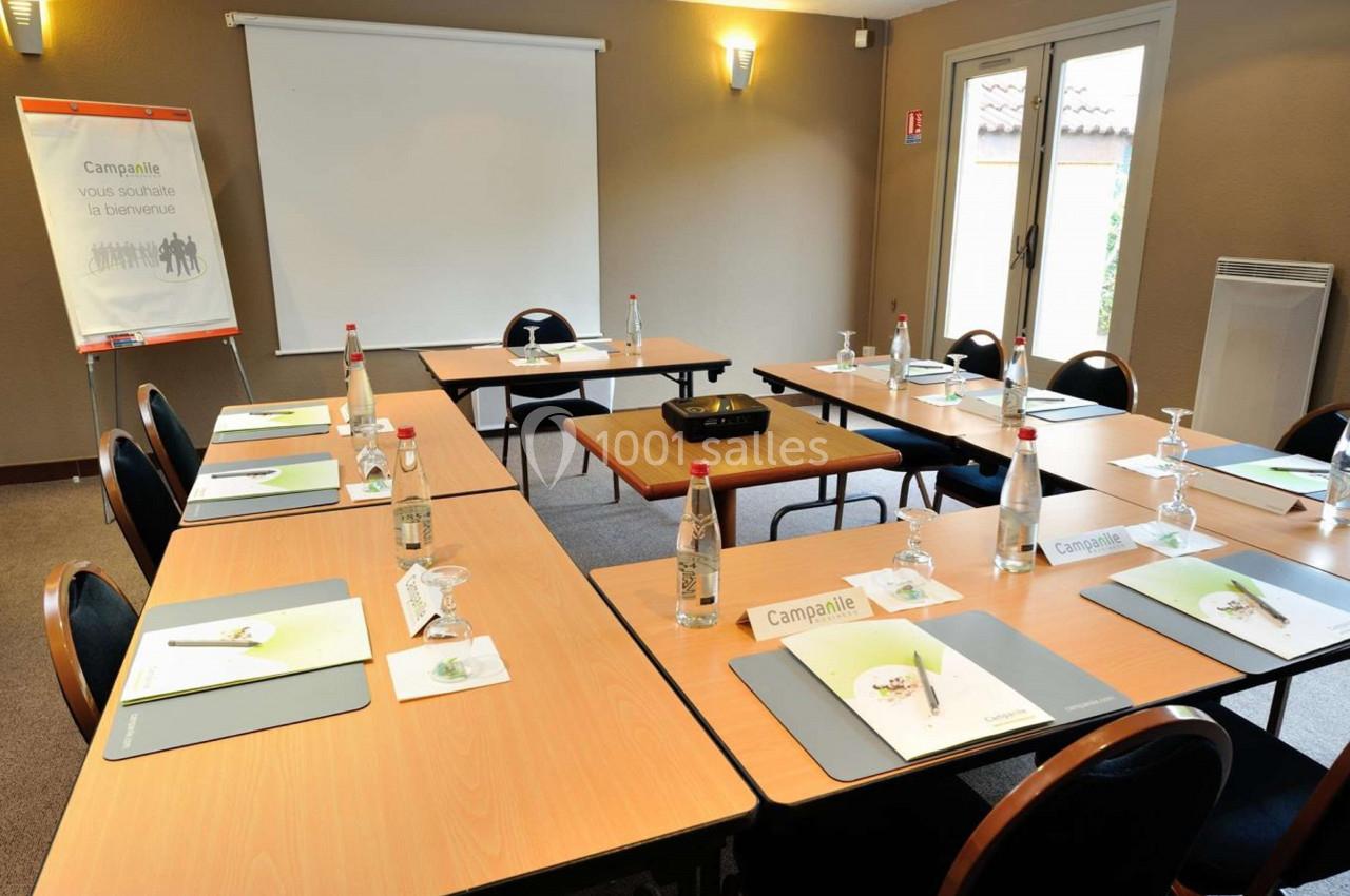 Salle de réunion équipée avec tables disposées en U, chaises, bouteilles d'eau, documents et écran de projection.