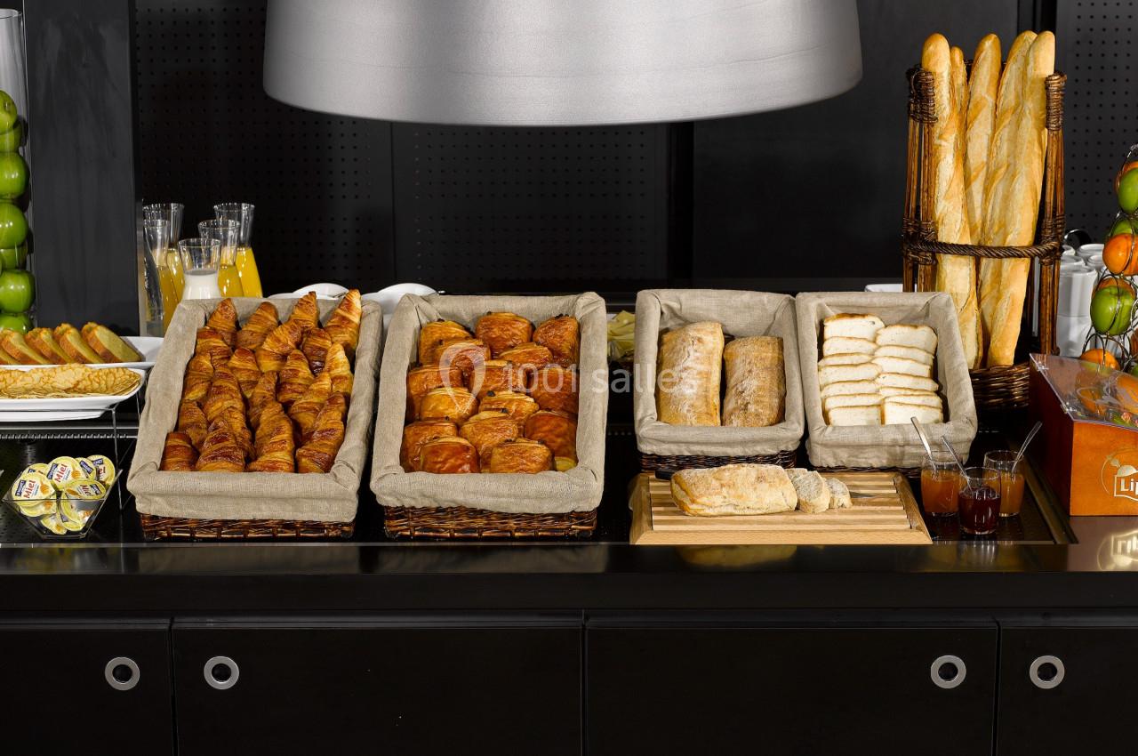 Buffet de viennoiseries et pains variés disposés dans des paniers en osier sur un comptoir noir.