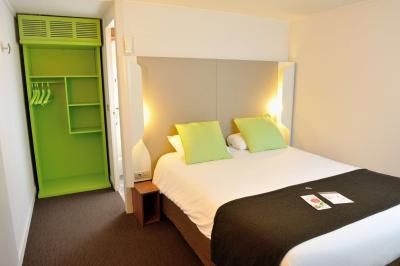 Bâtiment avec toit en tuiles, enseigne ’Campanile’, entouré de haies, d'arbustes et d'un olivier sous un ciel dégagé.