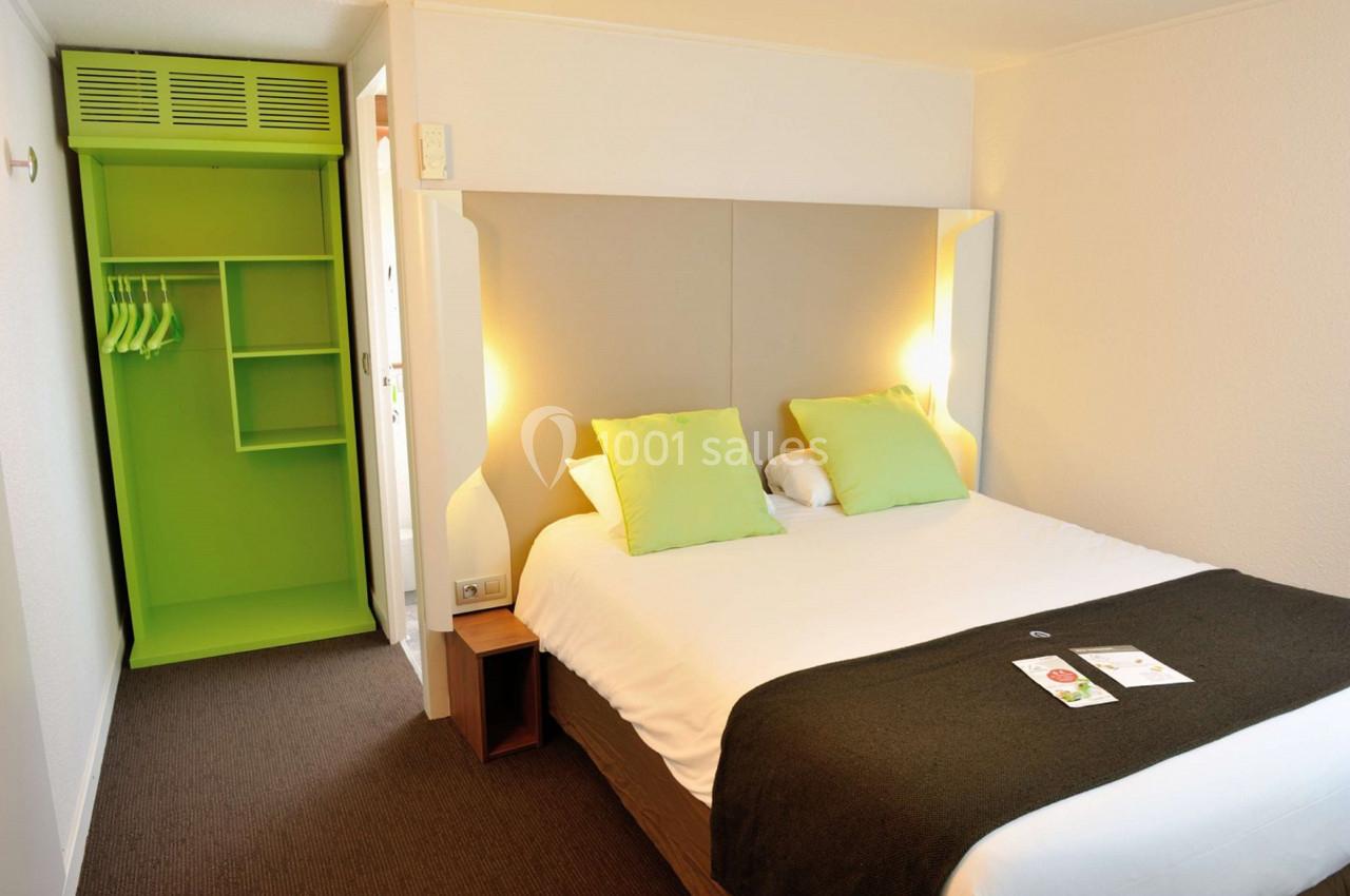 Chambre d'hôtel avec lit double, oreillers verts, armoire ouverte verte et éclairage doux.