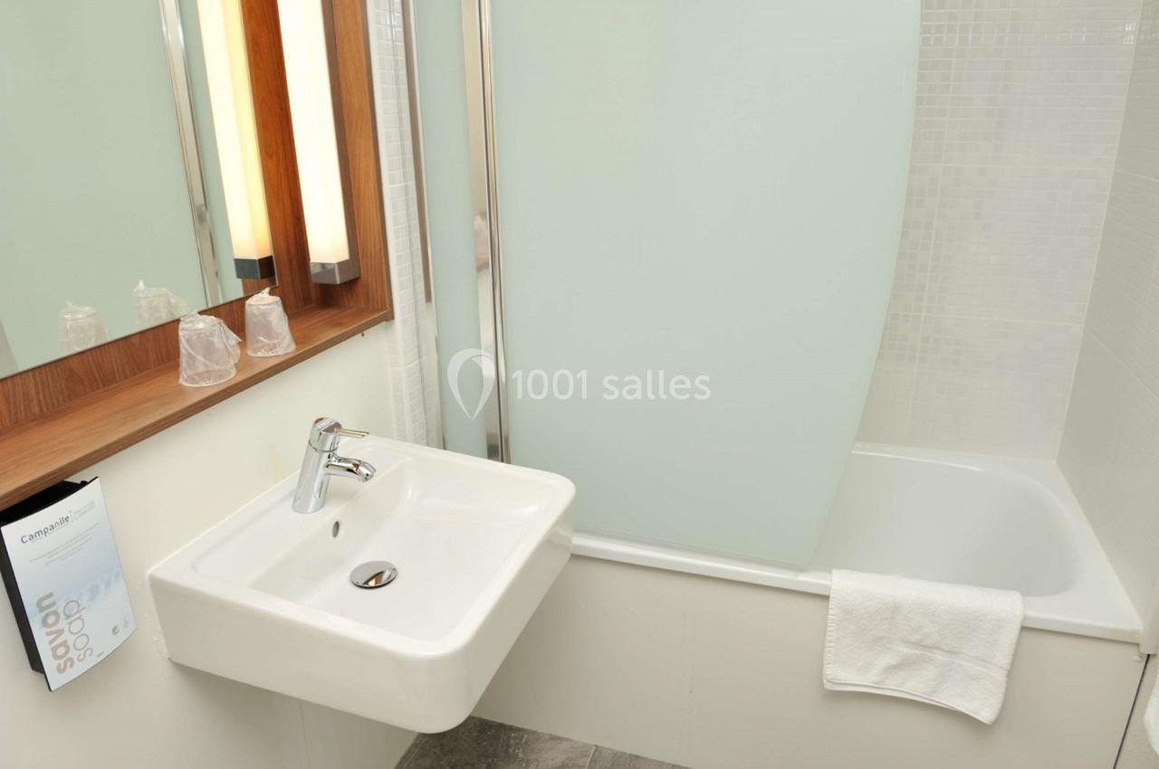 Lavabo blanc avec miroir en bois, baignoire avec paroi vitrée et serviette blanche posée sur le bord.