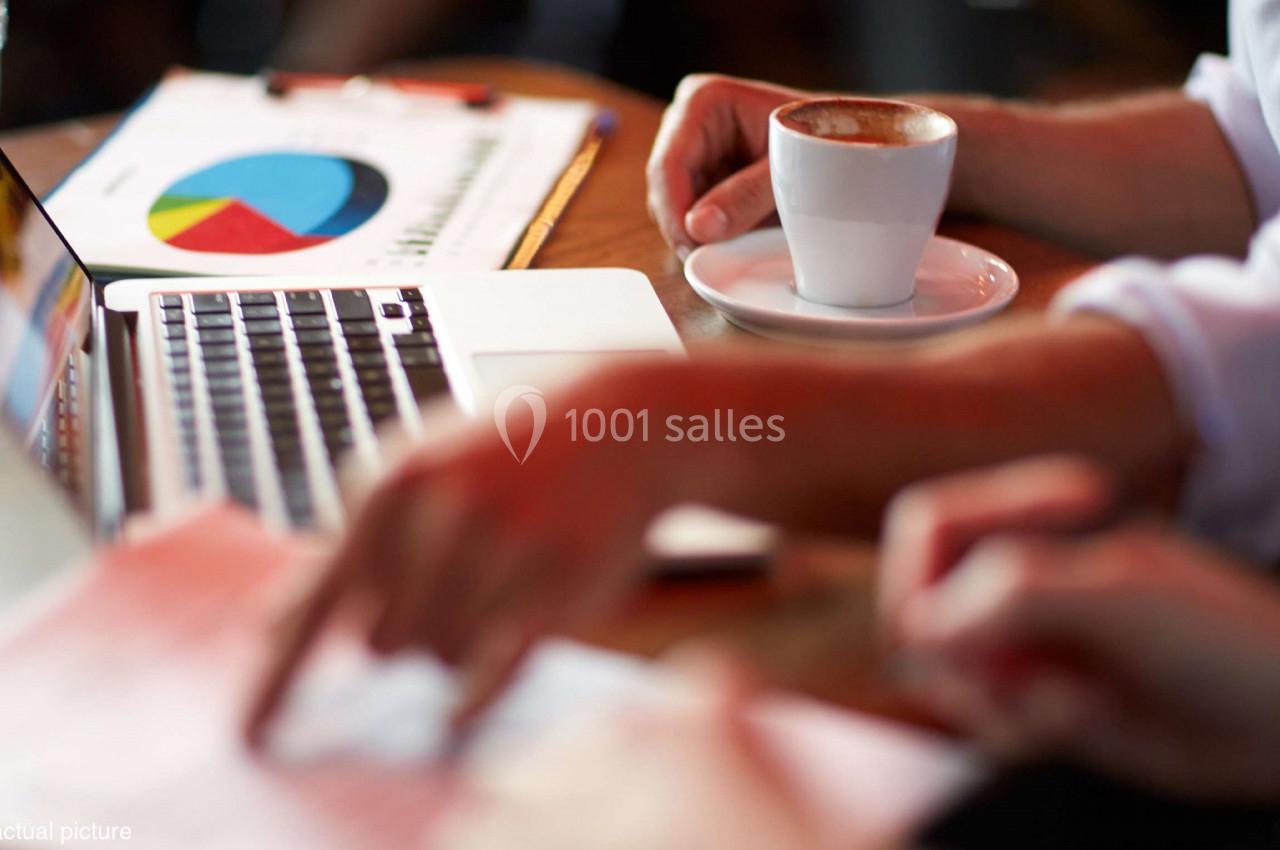 Deux personnes travaillent sur un ordinateur portable avec des documents et un café sur une table.