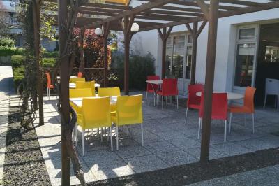 Bâtiment avec toit en tuiles, enseigne ’Campanile’, entouré de haies, d'arbustes et d'un olivier sous un ciel dégagé.