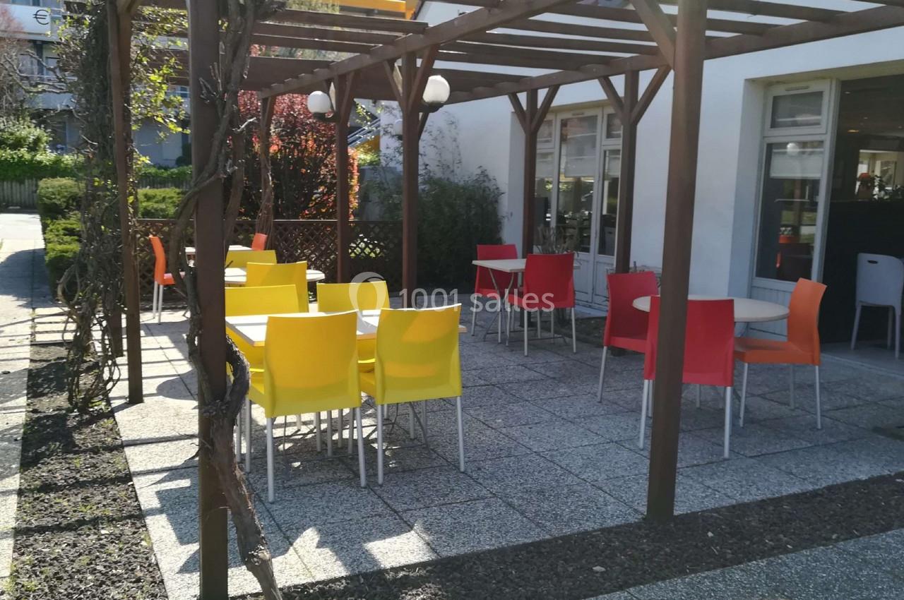 Terrasse extérieure avec tables et chaises colorées sous une pergola en bois, près d'un bâtiment vitré.