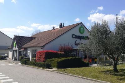 Bâtiment avec toit en tuiles, enseigne ’Campanile’, entouré de haies, d'arbustes et d'un olivier sous un ciel dégagé.