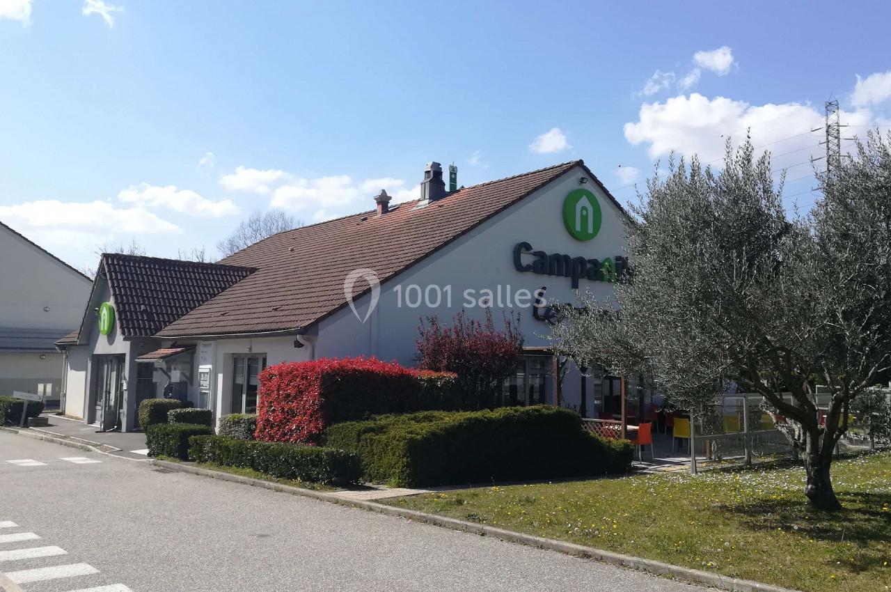 Bâtiment avec toit en tuiles, enseigne ’Campanile’, entouré de haies, d'arbustes et d'un olivier sous un ciel dégagé.