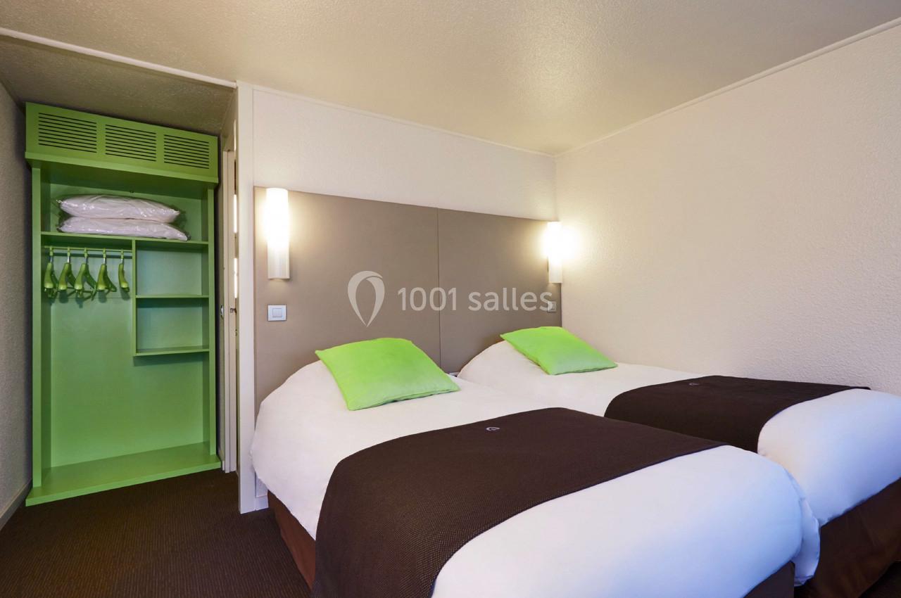 Deux lits simples avec oreillers verts dans une chambre d'hôtel, armoire ouverte avec cintres et étagères.