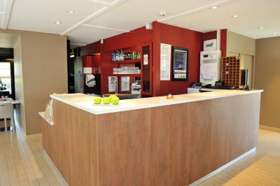 Bâtiment avec toit en tuiles, enseigne ’Campanile’, entouré de haies, d'arbustes et d'un olivier sous un ciel dégagé.