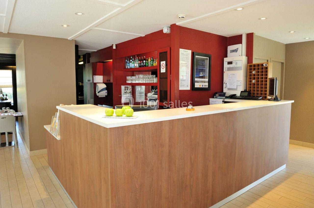 Comptoir d'accueil en bois clair avec des étagères de boissons en arrière-plan dans un espace lumineux.