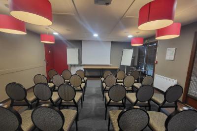 Salle de réunion avec chaises empilées, tables disposées en rangées et luminaires rouges suspendus.