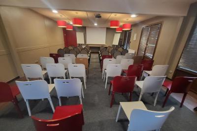 Salle de réunion avec chaises empilées, tables disposées en rangées et luminaires rouges suspendus.
