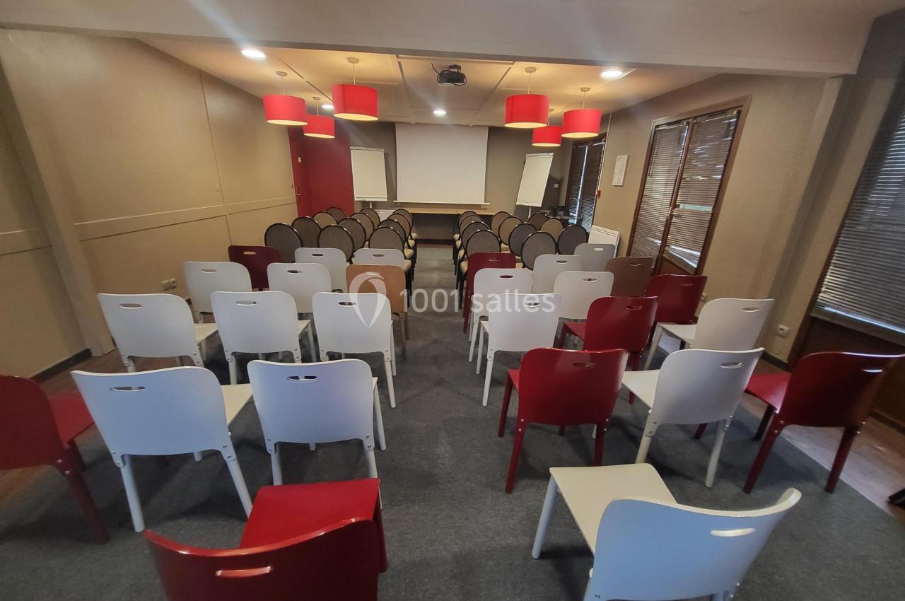 Salle de conférence avec des rangées de chaises blanches et rouges face à un écran de projection et deux tableaux blancs.