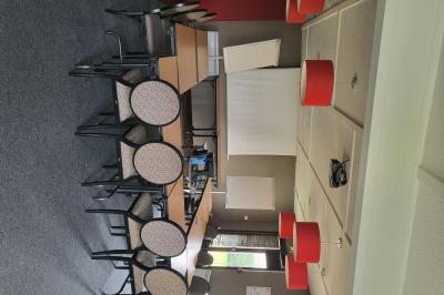 Salle de réunion avec chaises empilées, tables disposées en rangées et luminaires rouges suspendus.