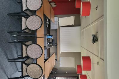 Salle de réunion avec chaises empilées, tables disposées en rangées et luminaires rouges suspendus.