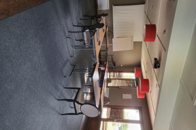 Salle de réunion avec chaises empilées, tables disposées en rangées et luminaires rouges suspendus.