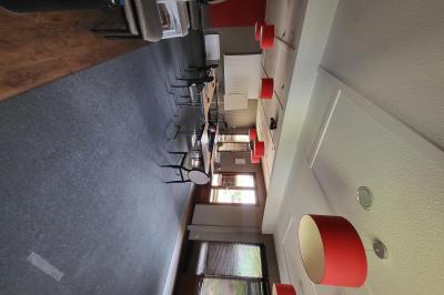 Salle de réunion avec chaises empilées, tables disposées en rangées et luminaires rouges suspendus.