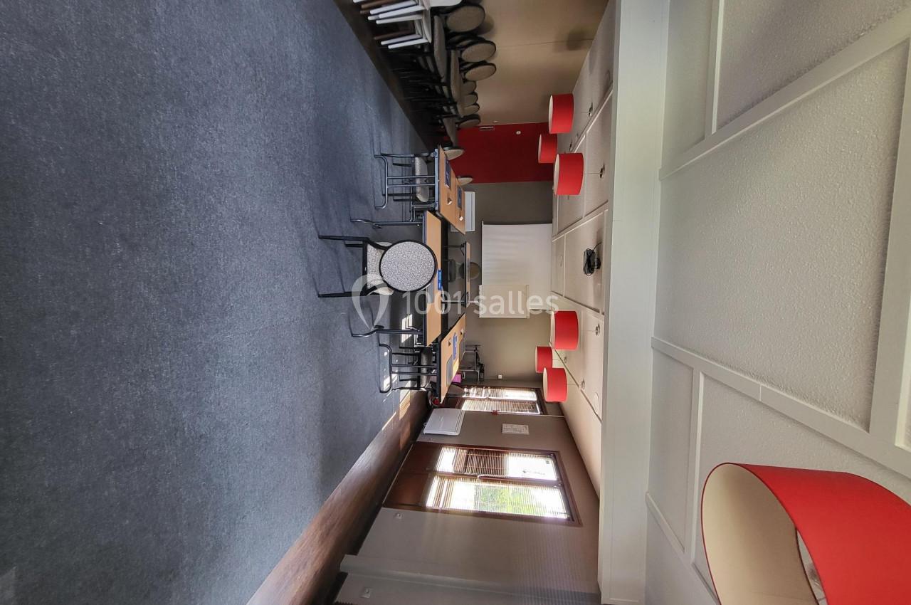 Salle de réunion lumineuse avec tables, chaises, murs clairs et lampes rouges suspendues.