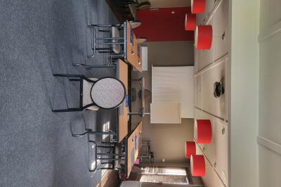 Salle de réunion avec chaises empilées, tables disposées en rangées et luminaires rouges suspendus.
